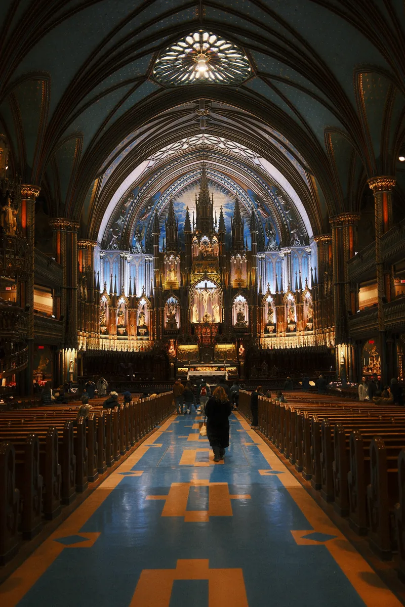 The blue and gold nave of Notre-Dame Basilica in Montréal, a lone visitor walking up the aisle